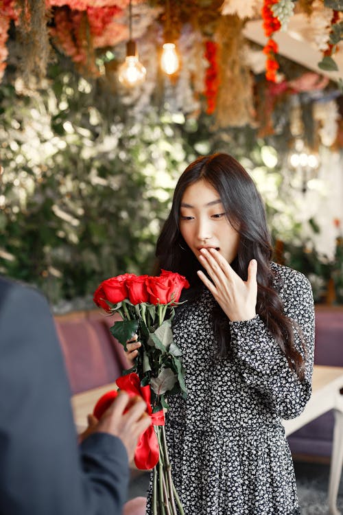 A Woman in Floral Dress Holding a Bunch of Red Roses