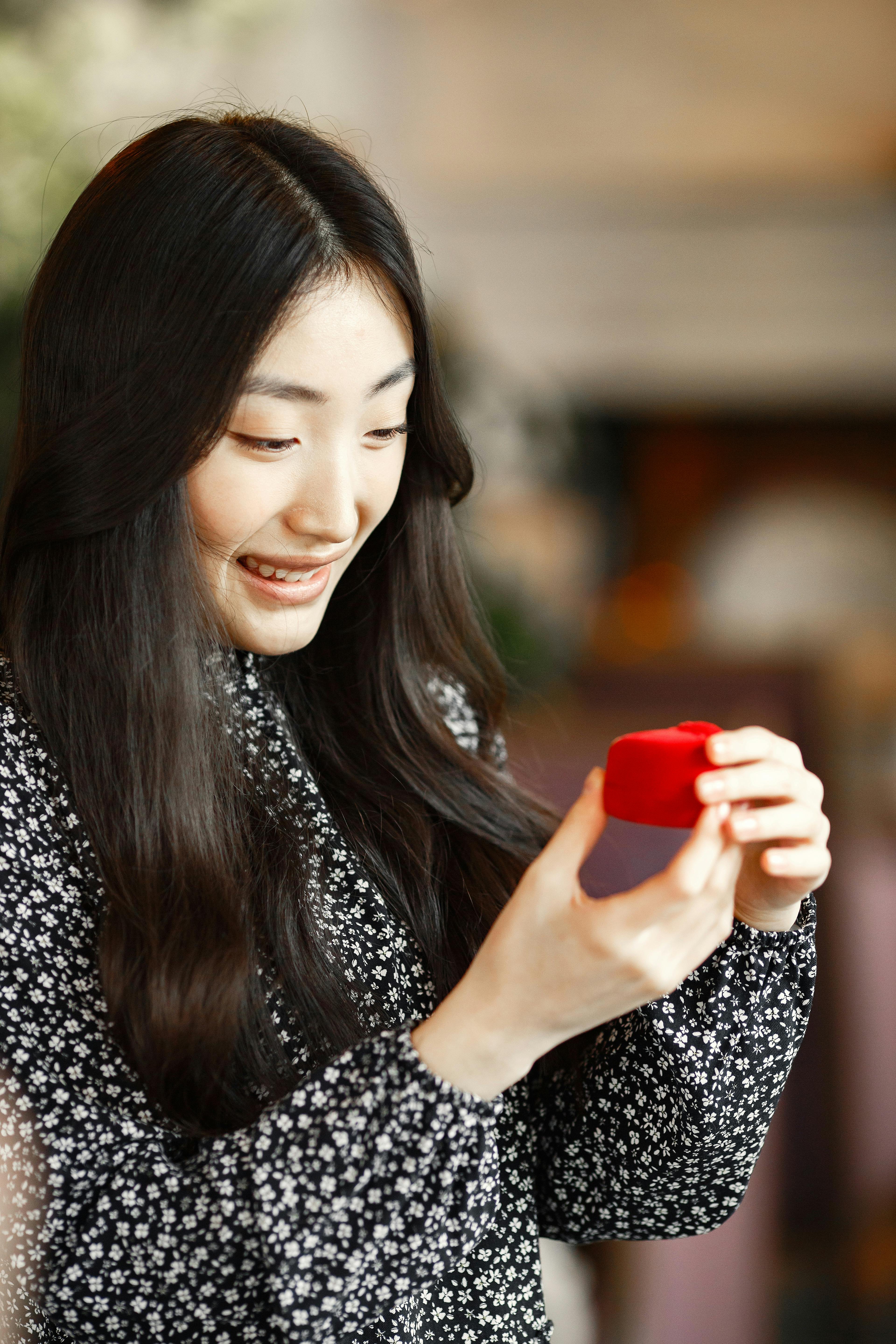 A happy woman excitedly holds a small red ring box, symbolizing a special moment.