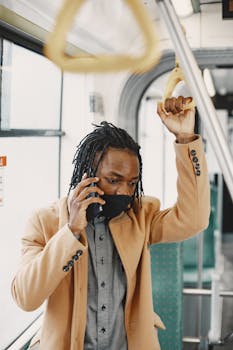 A man wearing a face mask talks on the phone while standing in a public bus.