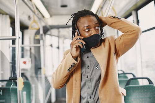 Young Man in Face Mask Talking on Phone in Bus