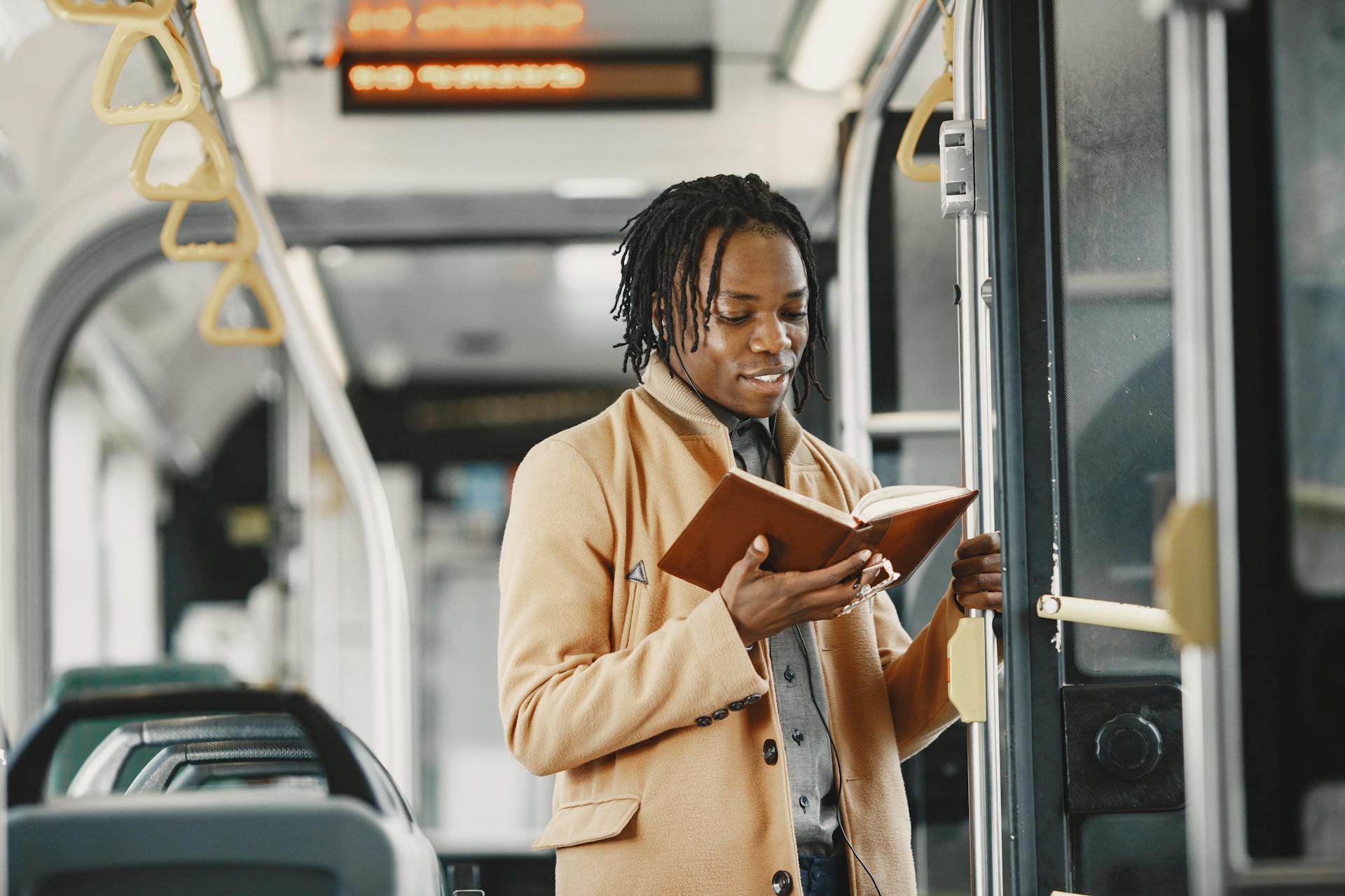 Man reading a book while standing inside a bus. Urban commuting scene with an interior focus.