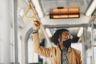 Man in Brown Coat Wearing Facemask and Eyeglasses Holding on Bus Handle