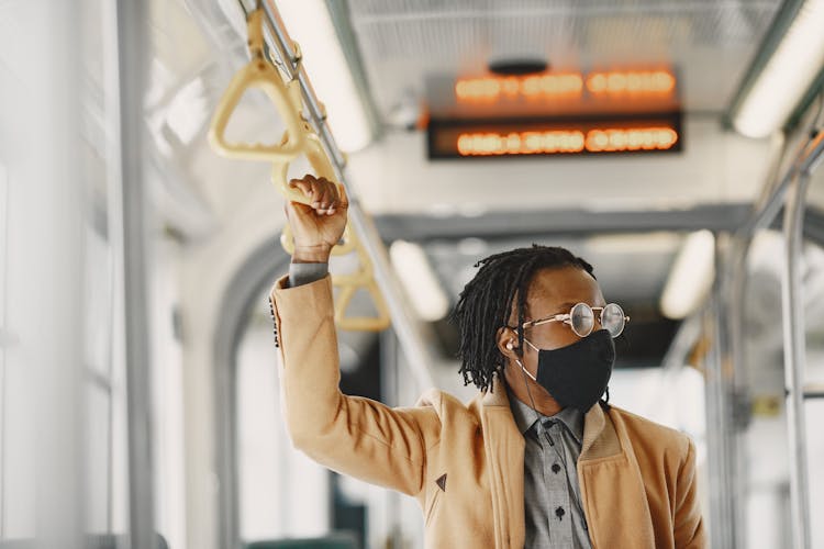 Man In Brown Coat Wearing Facemask And Eyeglasses Holding On Bus Handle 