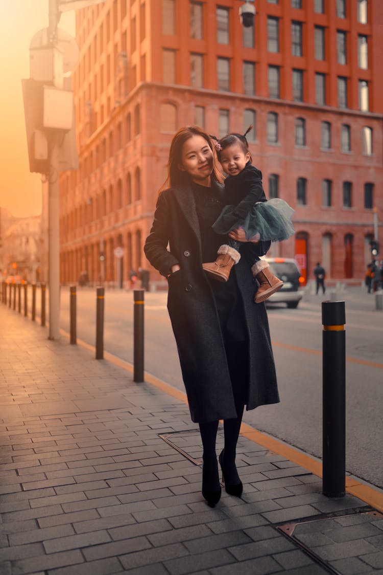 Woman In Black Coat Holding Her Baby On Sidewalk