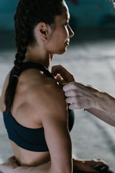 Close-up of a woman athlete receiving kinesio tape on her shoulder indoors.