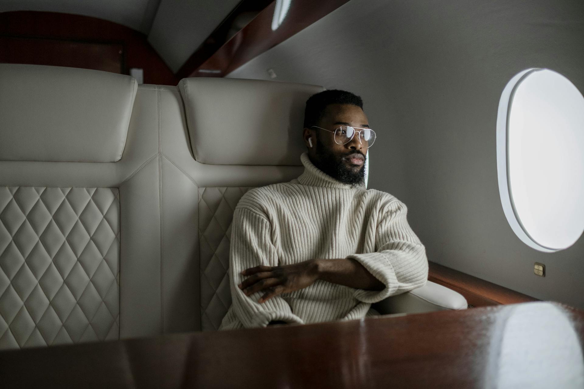 A stylish man in a turtleneck relaxes inside a private jet, embodying luxury travel.