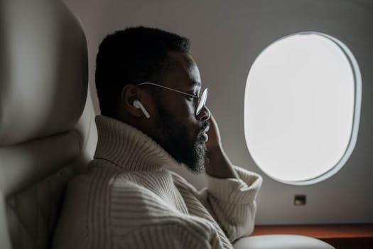 A businessman listening to music on an airplane, sitting by the window in a cozy sweater.