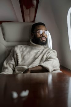Businessman with a beard and glasses relaxing in an airplane seat, gazing out the window during flight.