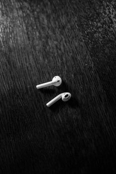 Black and white close-up of wireless earphones on a wooden surface, showcasing minimalist technology design.