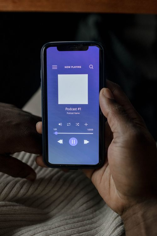 Free Hand holding a smartphone streaming a podcast with music controls visible. Stock Photo