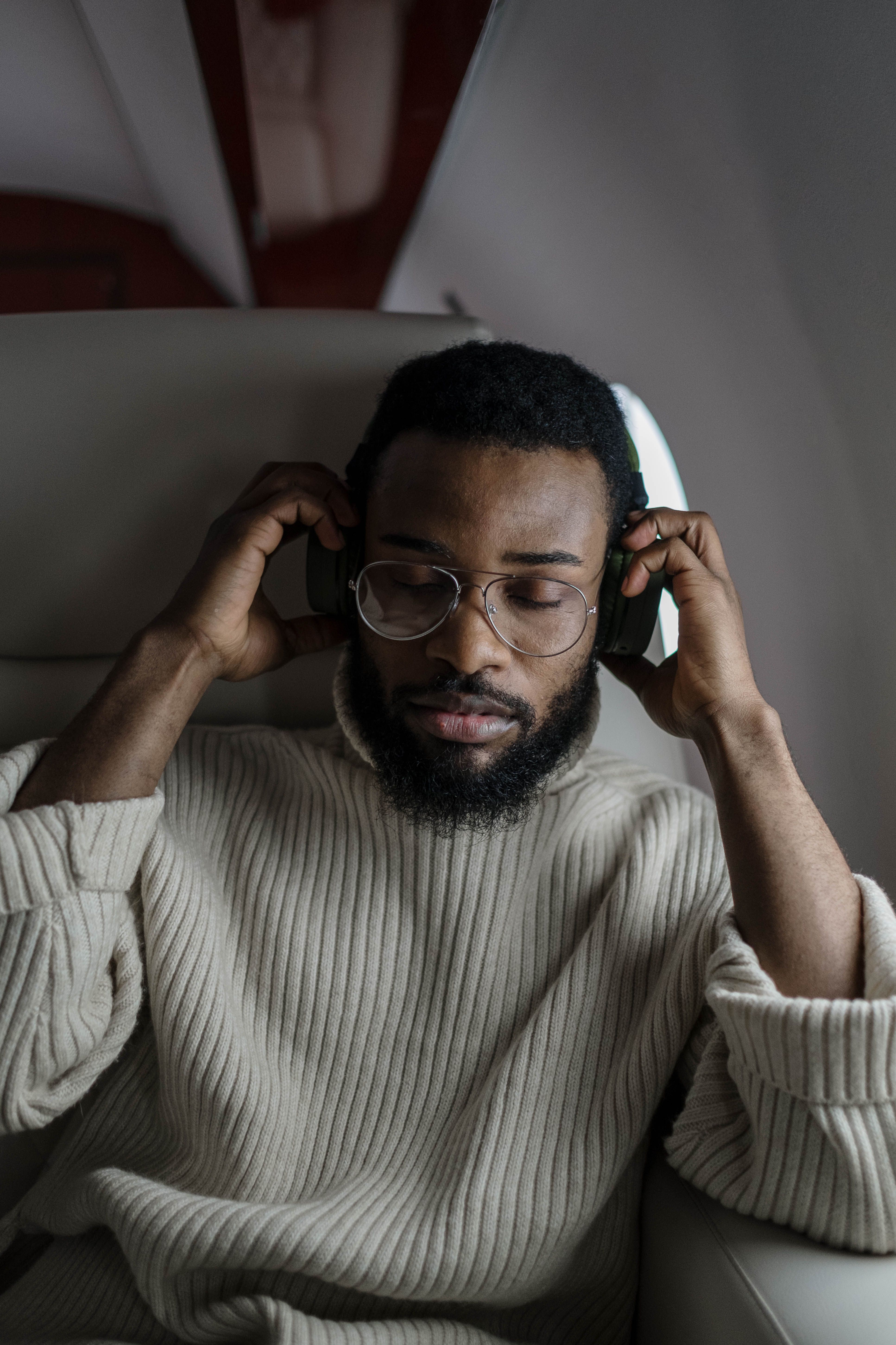 A man wearing over-ear headphones with his eyes closed, listening to music during a flight.