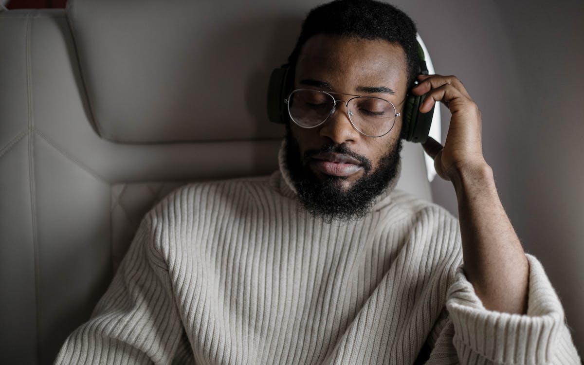 A man in a sweater enjoys music with headphones while sitting on an airplane.
