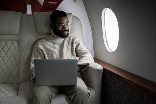 A man wearing headphones uses a laptop in a luxurious airplane cabin.