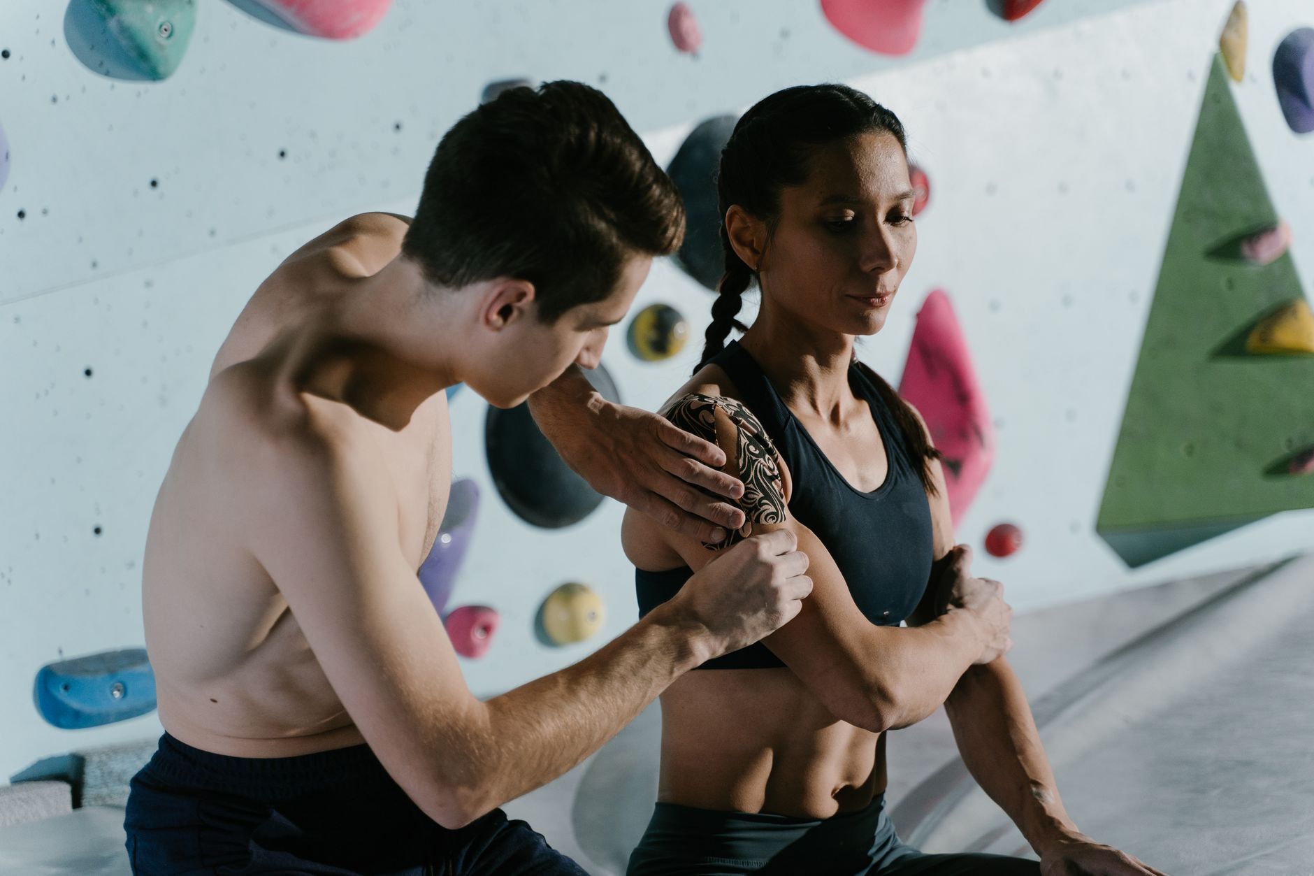 Climber wrapping fingers with athletic tape on a sunny outdoor crag, showing tape roll nearby.