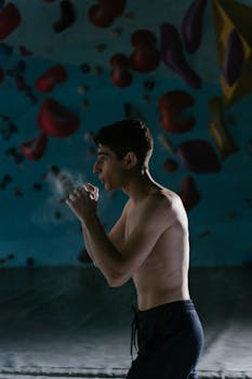 A shirtless man prepares with talc before climbing in an indoor gym.