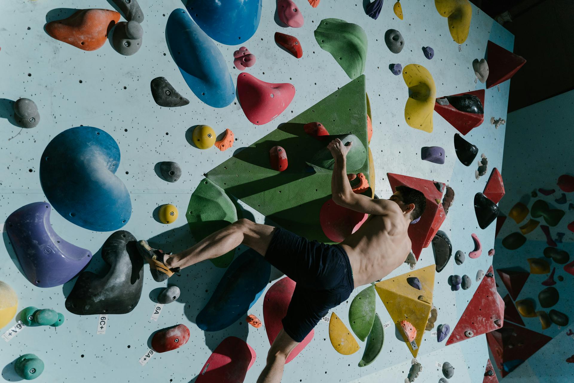 A man climbs a colorful, challenging bouldering wall at an indoor gym, focused on training.
