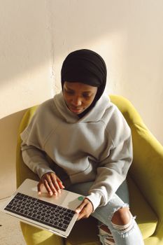 African woman in hijab sitting on a chair using a laptop. High angle view in daylight.