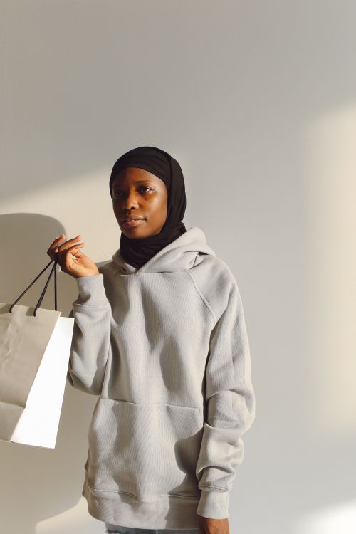 Free Side view of a black woman in a hoodie holding a shopping bag indoors. Stock Photo