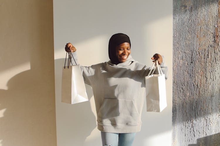 Portrait Of A Woman In Black Headscarf With Paper Shopping Bags Against Bright Wall