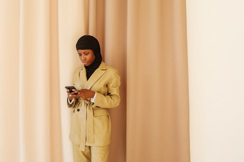 Woman in Beige Coat With Black Hajib Using Cellphone