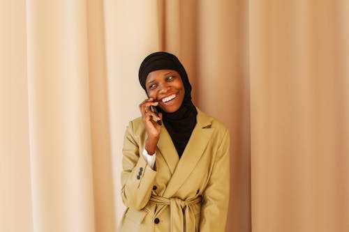 Free Smiling Woman in Beige Coat Talking Over the Phone Stock Photo