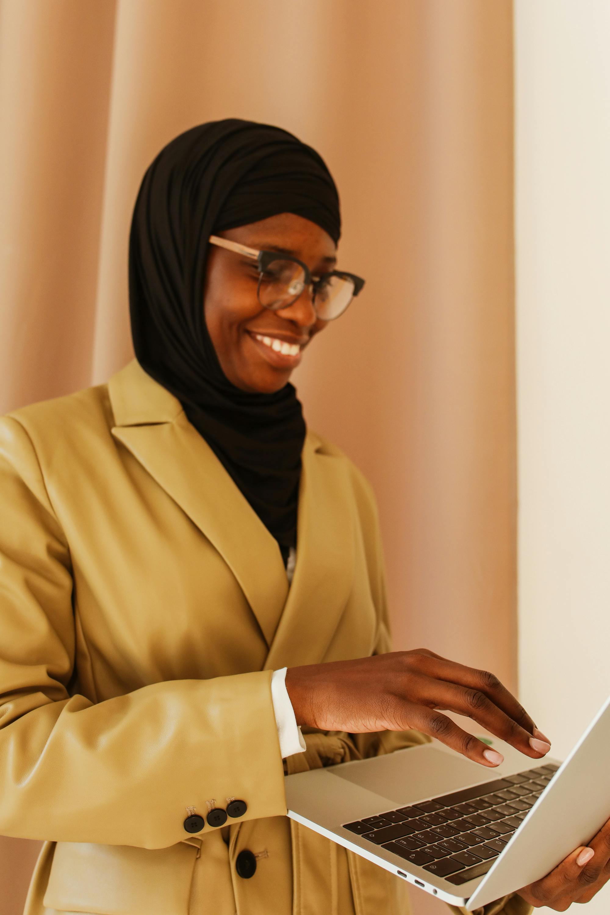 Smiling woman in hijab working on a laptop, demonstrating confidence and professionalism.