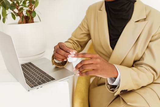 A person in a suit using AirPods while working on a laptop indoors.
