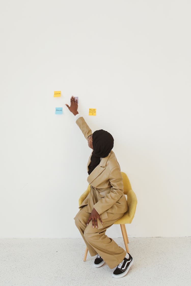 A Person Sitting On Chair Touching A Wall With Sticky Notes