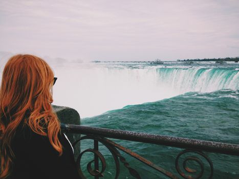 Woman views the majesty of Niagara Falls, a famous natural landmark, from a railing.