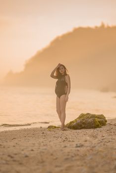 Serene image of a pregnant woman in a swimsuit standing on a beach during sunset.