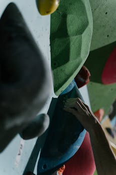 Close-up of a hand gripping colorful holds on an indoor climbing wall.