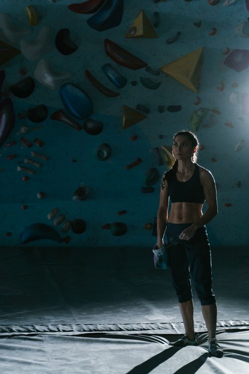 Free A woman stands in a dimly lit indoor bouldering gym, preparing to climb a wall. Stock Photo