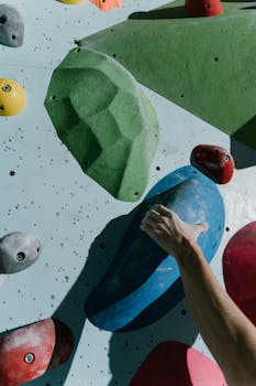 A hand grips colorful climbing holds on an indoor wall, showcasing athletic effort.