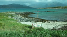 一艘帆船静静地停泊在沙滩海岸线上，背景是连绵的山脉