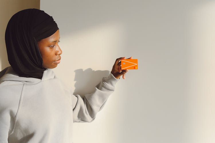 A Woman Wearing Black Hijab Holding Orange Credit Card