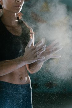 Close-up of athletic woman clapping hands with chalk powder in gym.