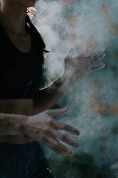 Close-up of a woman athlete's hands covered in chalk dust, captured in dramatic lighting.
