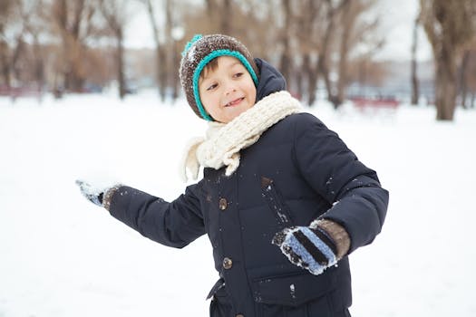 A happy child in a blue jacket playing with snow in a winter park.