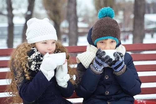 Girl and Boy Drinking while Sitting on a Bench During Winter Season