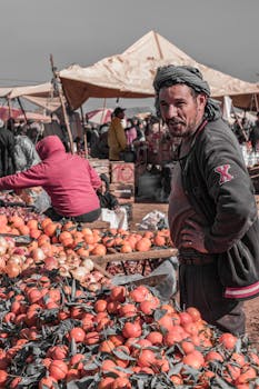 A local vendor stands by his stall of oranges at a bustling outdoor market, surrounded by vibrant activity.
