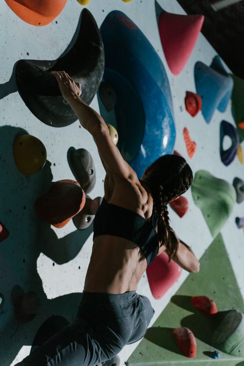 Free A female climber tackles a challenging indoor rock wall under strong lighting, showcasing strength and focus. Stock Photo