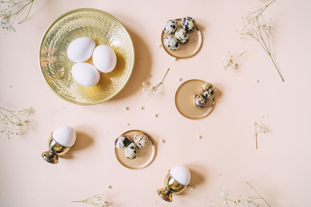 artistic flat lay of chicken and quail eggs on gold coasters adorned w