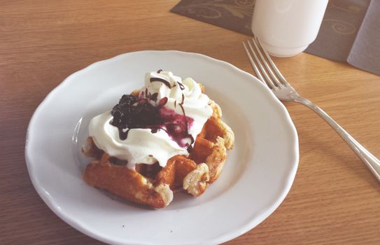 Mouthwatering waffle topped with blueberry sauce and whipped cream on a plate.