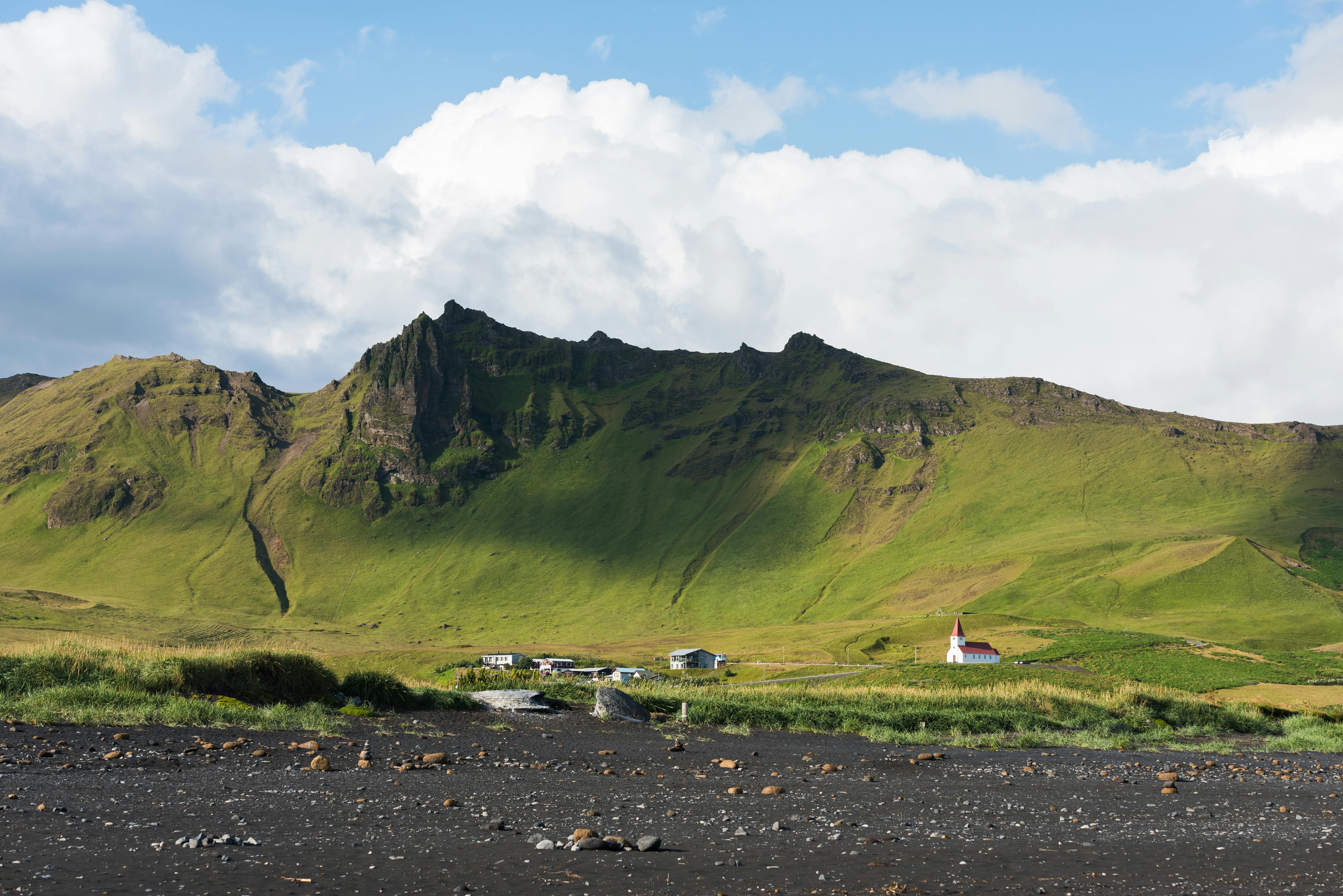 Beautiful Icelandic scenery showcasing a green mountain landscape with a distant church under a vibrant sky.