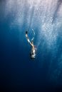 Anonymous female diver swimming under blue ocean in sunlight