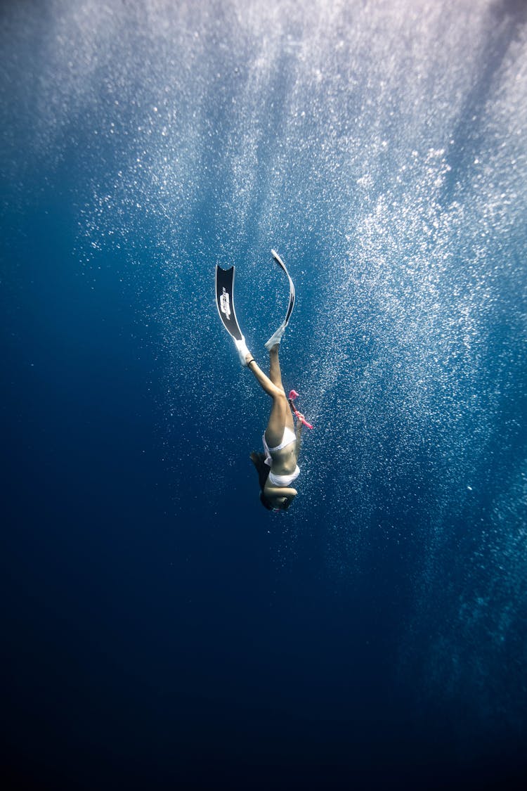 Anonymous Female Diver Swimming Under Blue Ocean In Sunlight