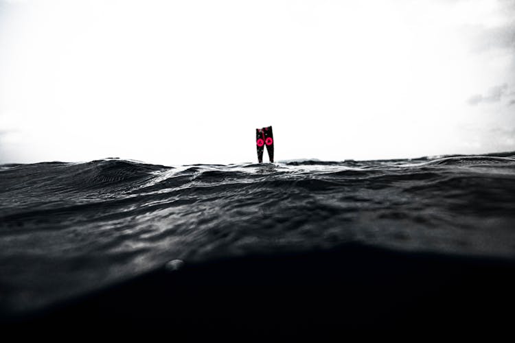 Flippers Of Anonymous Diver Over Wavy Sea Under Cloudy Sky