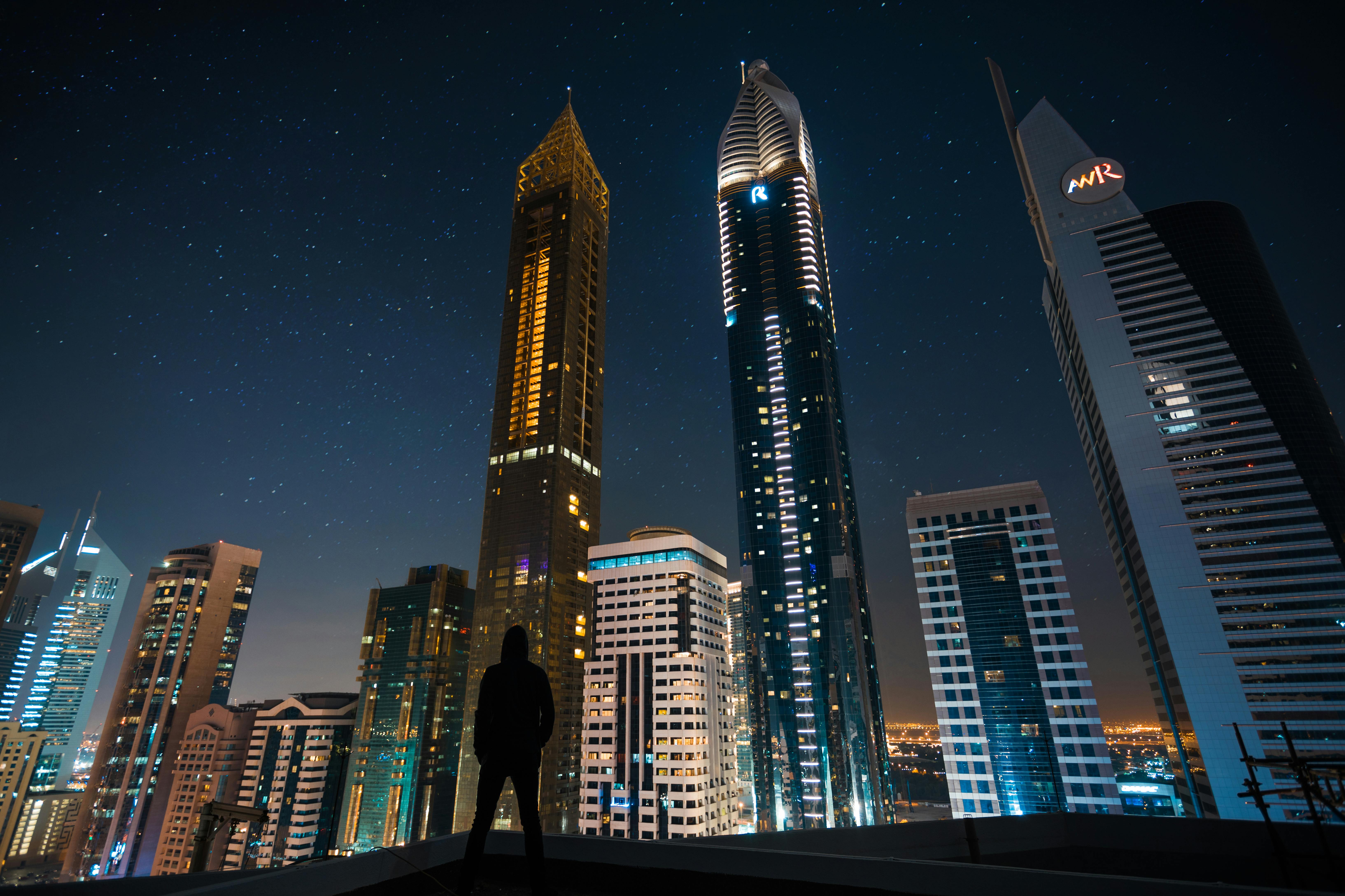 man standing in assorted building string light during night time