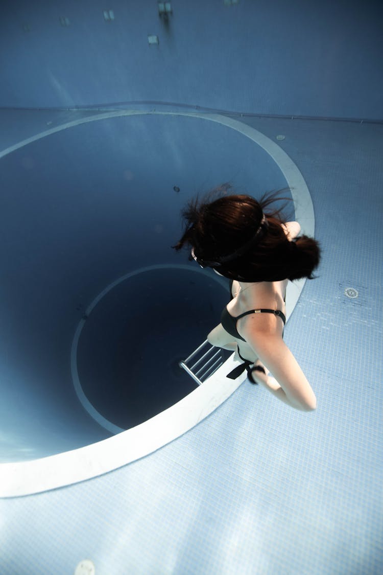 Anonymous Woman Swimming Underwater In Pool Near Round Hole