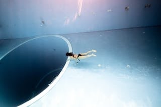 Unrecognizable lady swimming underwater in pool near big round hole